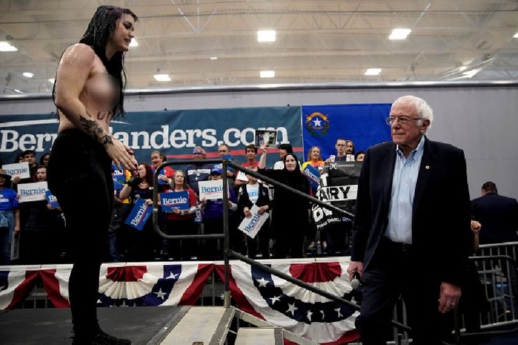 Calon presiden dari Partai Demokrat, Bernie Sanders, menatap seorang wanita bertelanjang dada yang sudah mengganggu kampanyenya di Nevada pada Minggu (16/2/2020).