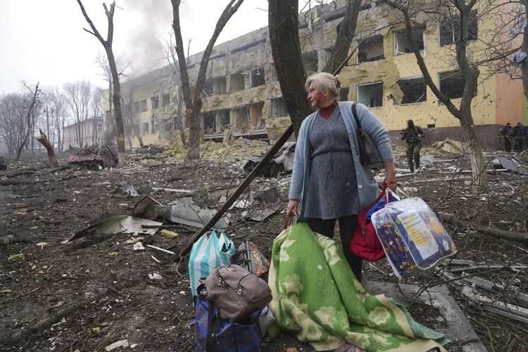 Seorang wanita berjalan di luar rumah sakit bersalin yang rusak akibat penembakan di Mariupol, Ukraina, Rabu, 9 Maret 2022. 