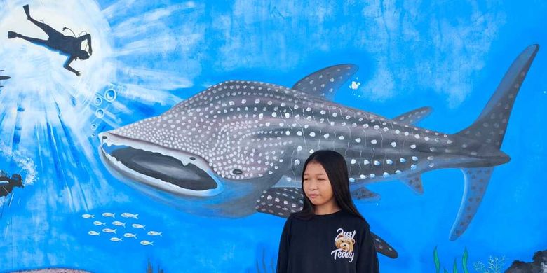 Sri Rahayu Ali di depan lukisan mural hiu paus di pantai Botubarani, Gorontalo, Rabu (3/4/2024). Gadis berumur 12 tahun kelas 6 SD ini memiliki pengalaman interaksi menarik dengan hiu paus. 