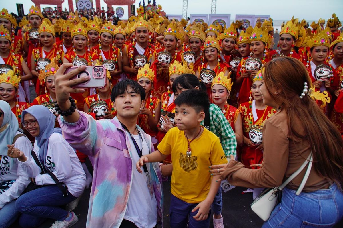 Wisatawan mancanegara asyik mengabadikan momen dalam Festival Segoro Topeng Kaliwungu di Pantai Watu Pecak Lumajang, Minggu (29/6/2025)