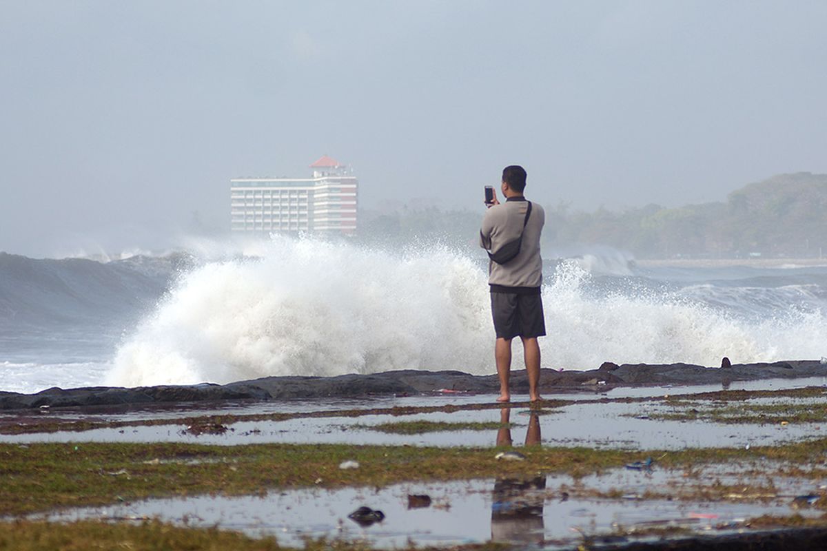 Warga menyaksikan gelombang tinggi di kawasan Pantai Padang Galak, Denpasar, Bali, Rabu (25/7/2018). Gelombang tinggi yang terjadi di Bali sejak seminggu terakhir mengakibatkan pelarangan aktivitas kapal cepat melalui Pantai Sanur dan Pelabuhan Padangbai serta merusak sejumlah pura di Bali.