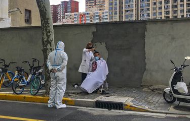 Seorang pekerja dengan alat pelindung menyaksikan seorang tukang cukur memotong rambut seorang warga Selasa, 31 Mei 2022, di Shanghai, China. 