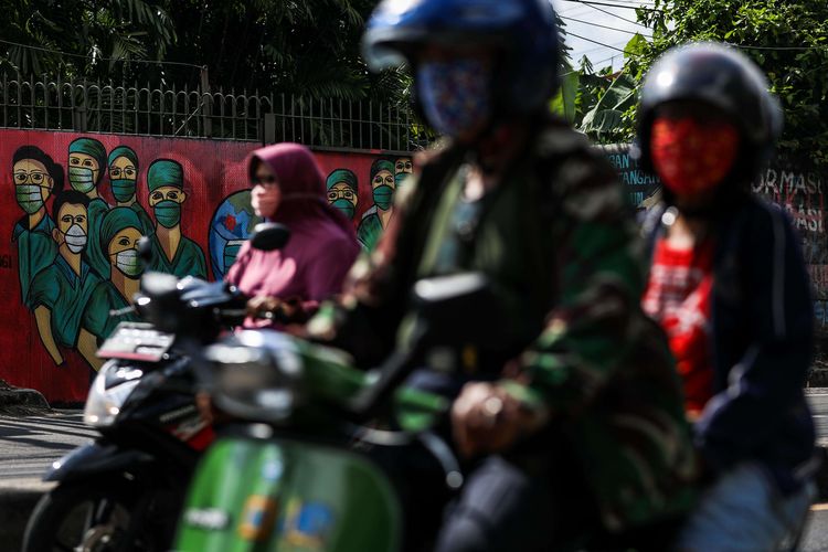 Warga menggunakan masker saat mengendarai sepeda motor melintas di depan mural tentang pandemi virus corona atau COVID-19 di Jalan Raya Jakarta-Bogor, Depok, Jawa Barat, Selasa (7/4/2020). Mural tersebut ditujukan sebagai bentuk dukungan kepada tenaga medis yang menjadi garda terdepan dalam menghadapi COVID-19 di Indonesia.