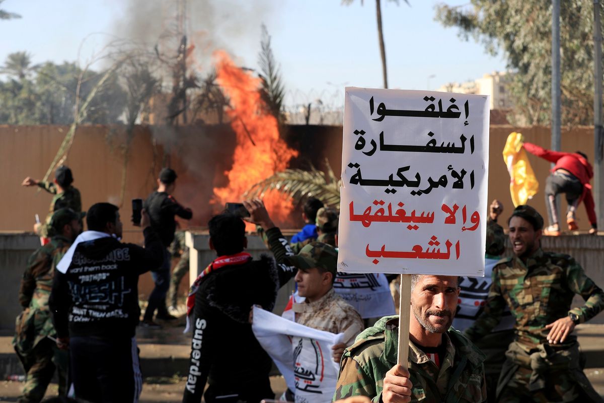 Seorang milisi Hashed al-Shaabi membentangkan poster bertuliskan tutup Kedutaan Besar AS, atau rakyat yang akan menutupnya di Kedutaan Besar AS di Baghdad, Irak, pada 31 Desember 2019. Demonstrasi itu terjadi buntut serangan udara AS yang menewaskan 25 milisi Hashed pekan lalu.