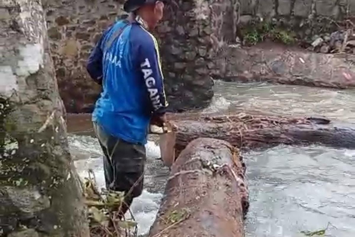 Petugas BPBD Kabupaten Pasuruan sedang memotong batang pohon yang menjadi penyebab meluapnya sungai Mukibat di Jjalan raya Surabaya-Malang di Kecamatan Purwosari, Kabupaten Pasuruan, Jawa Timur, Sabtu (12/04/2025) 