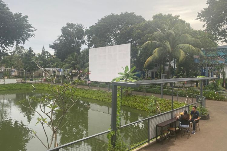 Layar putih di pinggir tengah danau buatan untuk Movie Night di CIBIS Park. 