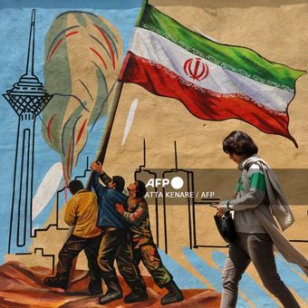 Seorang wanita Iran berjalan melewati mural anti-AS dan anti-Israel di Teheran pada 21 April 2026, di tengah gencatan senjata di wilayah tersebut.