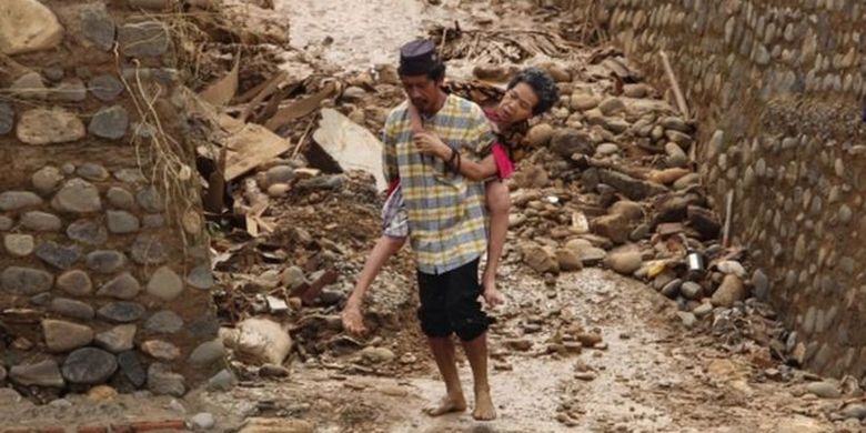 Seorang pria menggendong istrinya yang sedang sakit di tengah kondisi bencana di Desa Sukarame, Kecamatan Sajira, Kabupaten Lebak. 