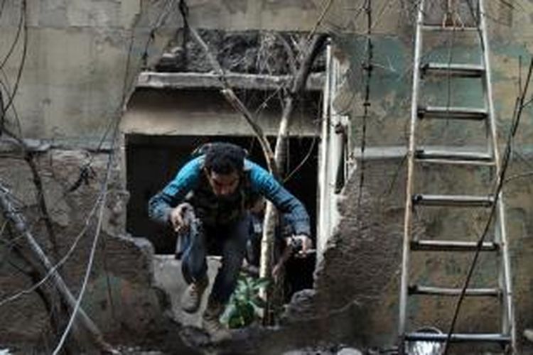 Seorang pemberontak Suriah merunduk melewati lubang di dinding untuk menghindari tembakan 
