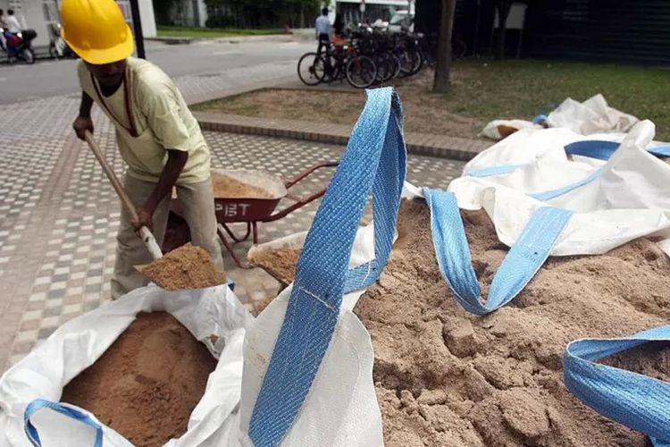 Seorang pekerja mengisi gerobak dorong dengan pasir di dekat lokasi konstruksi di Singapura.