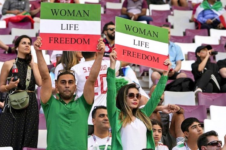Sejumlah supporter Iran dengan jersi bernuansa warna bendera Iran (merah, putih dan hijau), memegang poster dengan slogan bertuliskan ?Wanita. Kehidupan. Kebebasan? dan ?Kebebasan untuk Iran? di Piala Dunia Qatar 2022.
