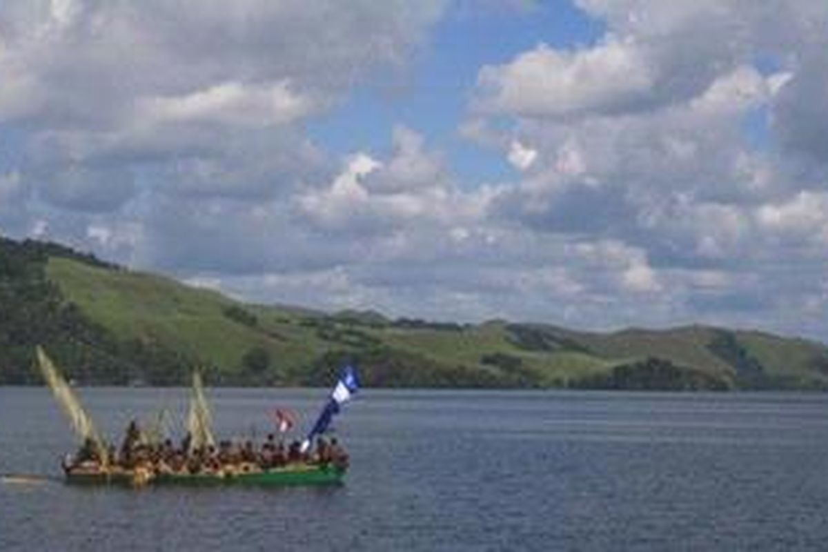 Perahu berlayar di tengah Danau Sentani dengan latar belakang pegunungan Cyclops