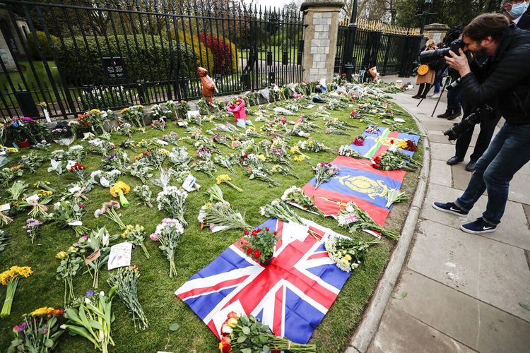 Bendera dibentangkan di antara bunga-bunga di luar Kastil Windsor di Windsor, Inggris setelah pengumuman mengenai kematian Pangeran Philip dari Inggris, Jumat 9 April 2021.