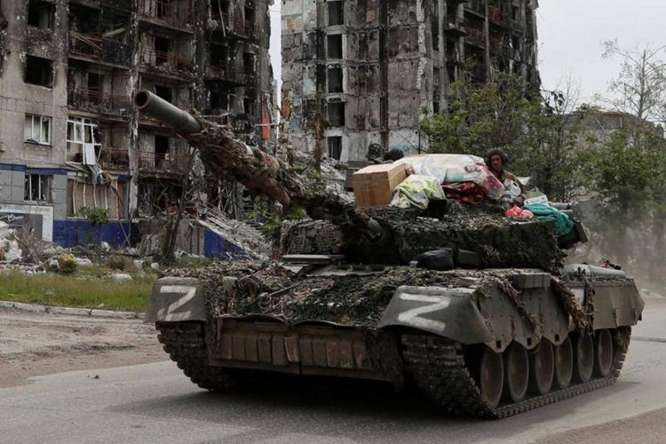 Gambar yang diambil pada akhir Mei menunjukkan tank bergerak melewati bangunan tempat tinggal yang dibom di kota Popasna, dengan sejumlah barang rumah tangga di atasnya.
