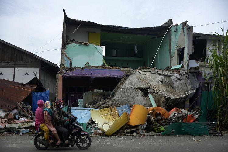 Motorists pass around a house damaged by an earthquake in Mamuju Regency, West Sulawesi, Sunday (17/1/2021). The earthquake with a magnitude of 6.2 that occurred on Friday (15/1/2021) in the early hours of the morning resulted in 56 people dying and dozens of residents still displaced.