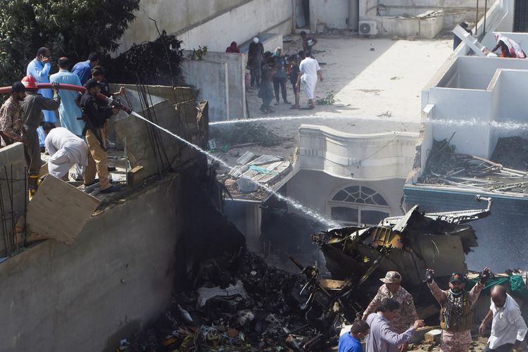 Polisi membantu menyemprotkan air untuk memadamkan api, akibat jatuhnya pesawat Pakistan International Airlines di permukiman Karachi, Jumat (22/5/2020). Lebih dari 100 orang tewas akibat insiden ini.