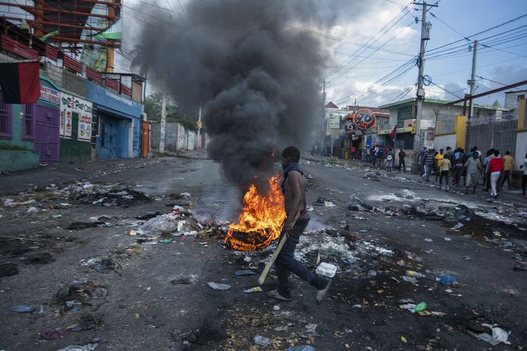 Seorang pria berjalan melewati ban yang dibakar oleh pengunjuk rasa selama protes menuntut pengunduran diri Perdana Menteri Ariel Henry di daerah Delmas Port-au-Prince, Haiti, Senin, 10 Oktober 2022.