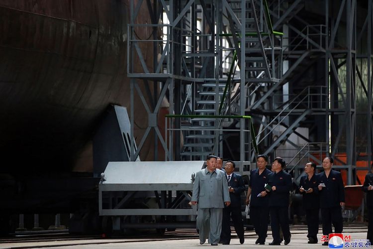 Pemimpin Korea Utara, Kim Jong Un (paling kiri), berjalan diikuti sejumlah pejabat, saat mengunjungi lokasi pembangunan kapal selam besar.