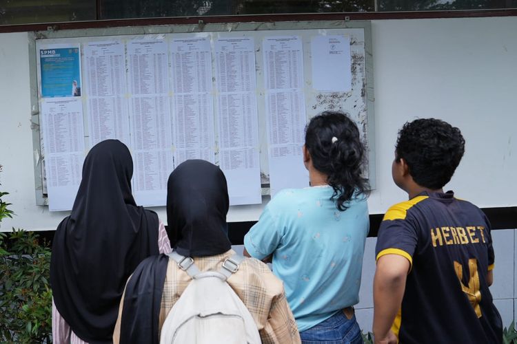 Orang tua dan siswa/i memeriksa daftar penerimaan sekolah di papan pengumuman.