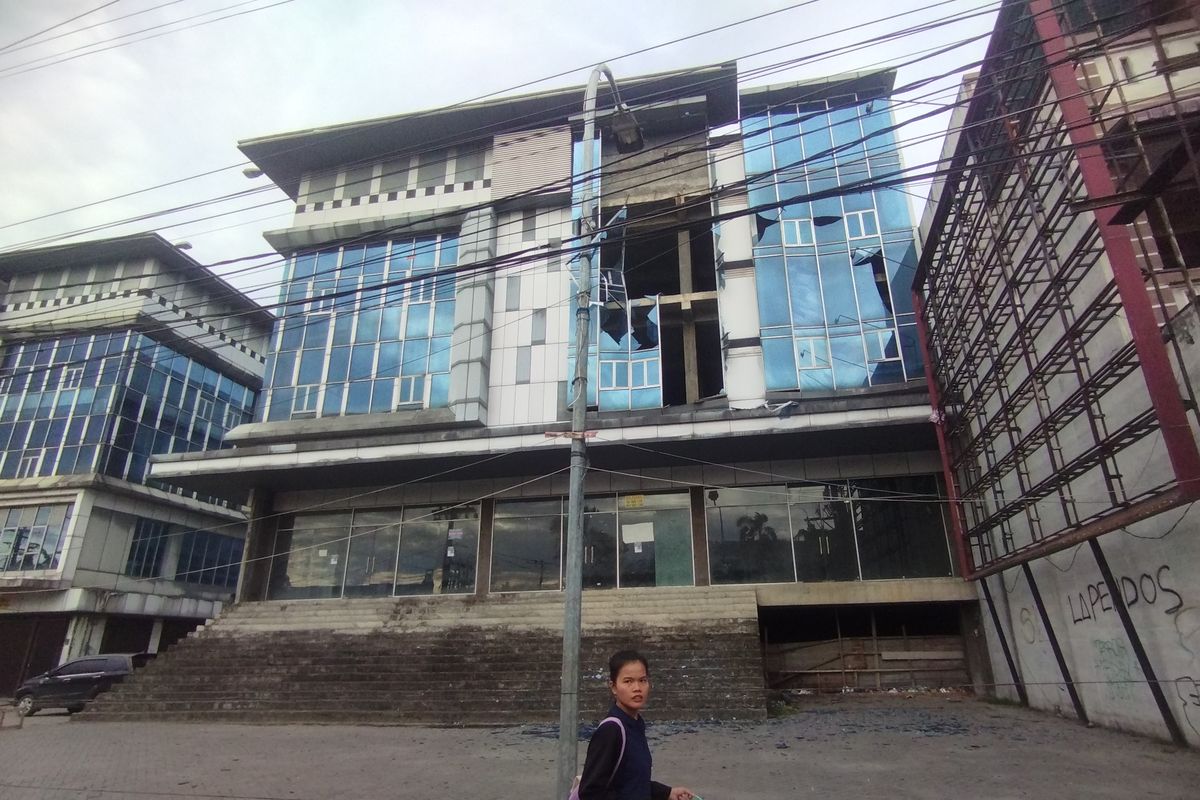 Seorang warga sedang melintas di depan bangunan kosong yang kacanya pecah berjatuhan setelah diterpa angin kencang di Jalan Kapten Muslim, Kecamatan Medan Helvetia pada Rabu (10/6/2025). (KOMPAS.COM/CRISTISON SONDANG PANE)