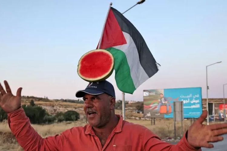 Seorang penjual semangka Palestina mengadakan pertunjukan untuk menarik pelanggan, di sebuah jalan di pintu masuk utara Kota Ramallah, pada 5 Juni 2023.
