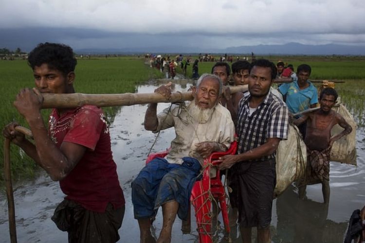 Pengungsi Rohingya dari Rakhine, Myanmar, memikul seorang kakek renta ketika melintasi perbatasan menuju Banglades.