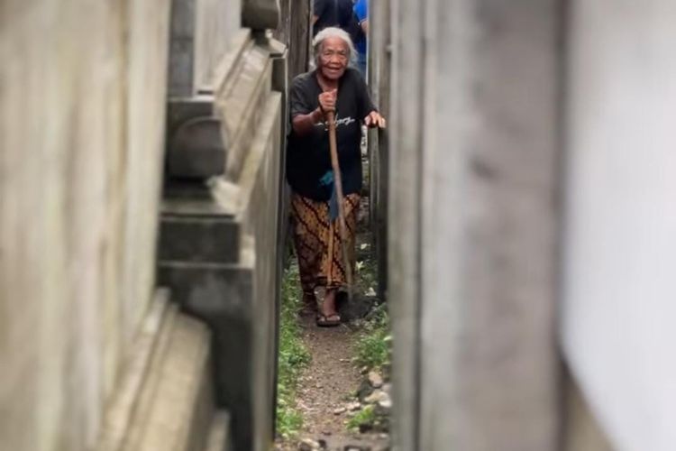 Seorang nenek yang berjalan dalam himpitan tembok pembatas GWK di Bali. 