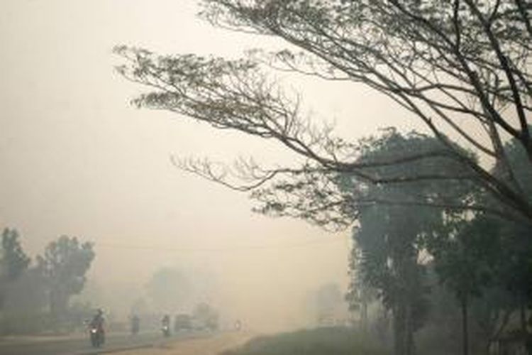 Pengendara melintasi jalan raya yang tertutup kabut asap dari kebakaran hutan dan lahan di Kampar, Riau, 4 September 2015. Kabut asap dari kebakaran hutan di Indonesia, mengakibatkan pembatalan penerbangan dan peringatan bagi warga untuk tetap tinggal di dalam rumah.