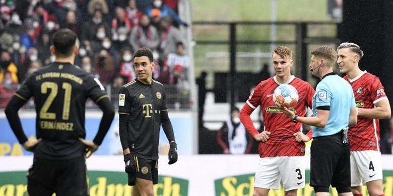 Wasit Christian Dingert berbicara dengan pemain Bayern Muenchen Lucas Hernandez dan Jamal Musiala. Laga Bundesliga 2021-2022 antara Freiburg vs Bayern Muenchen pada 2 April 2022 ini sempat terhenti karena tim tamu bermain dengan 12 pemain. 