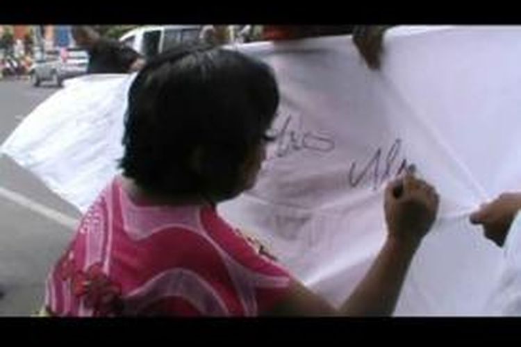Salah seorang pedagang di Pematangsiantar saat ikut membubuhkan nama dan tanda tangannya di kain putih yang disediakan mahasiswa yang berunjuk rasa menolak Pilkada lewat DPRD, Jumat (19/9/2014).