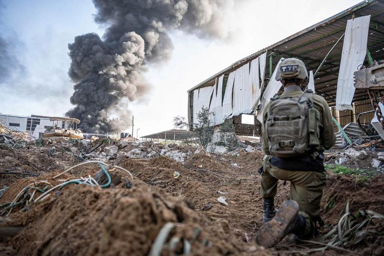 Foto selebaran yang dirilis oleh tentara Israel pada 19 Desember 2023 ini menunjukkan seorang tentara yang sedang beroperasi ketika asap mengepul di Jalur Gaza, di tengah pertempuran yang terus berlanjut antara Israel dan kelompok militan Palestina, Hamas. 