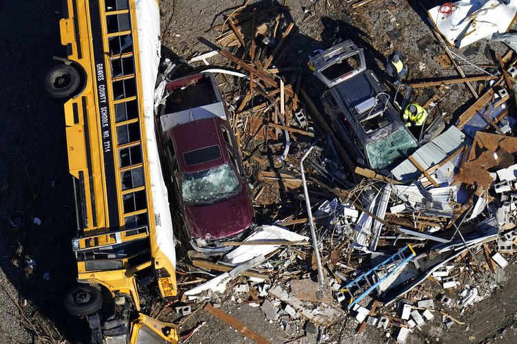 Dalam foto udara ini, sukarelawan tengah membersihkan puing-puing di dekat bus sekolah yang terbalik akibat tornado yang melanda wilayah Mayfield, negara bagian Kentucky, Amerika Serikat, Minggu (12/12/2021).