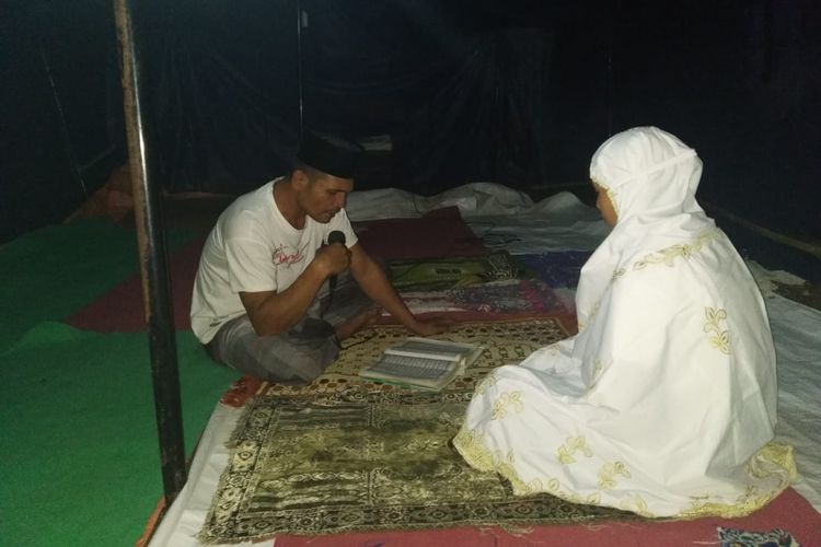 Dua warga Dusun Kebon Daye, Desa Pesanggrahan, Lombok  Timur, melakukan tadarus di tenda darurat dengan menggunakan hanya satu Al Quran, Senin (13/5/2019) malam. 