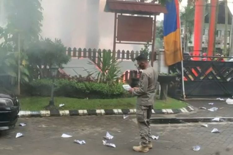 Salah satu anggota Satpol PP Kota Malang yang berjaga di rumah dinas wali kota saat memungut salah satu dari pesawat kertas yang dilempatkan ke halaman rumah dinas wali kota. (Foto: Tangkapan Layar dari Video yang Beredar).