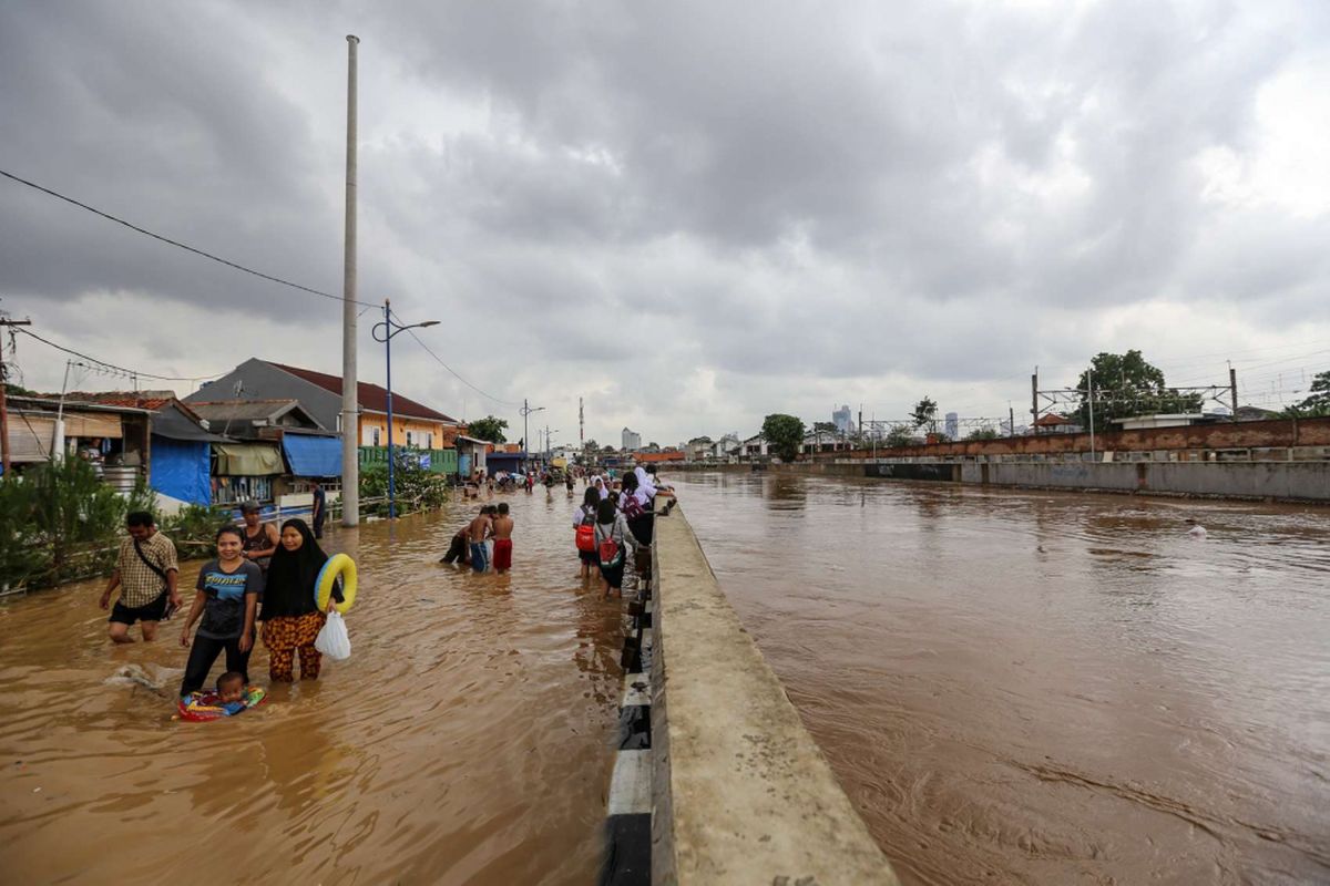 Warga berjalan melintasi banjir di Kampung Pulo, Jatinegara, Jakarta Timur, Selasa (6/2/2018). Banjir merendam ratusan rumah warga akibat luapan air dari Sungai Ciliwung.