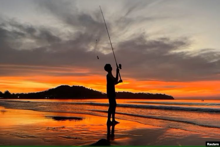 Seorang anak laki-laki memancing saat matahari terbenam di Pantai Bang Tao di Phuket, Thailand, 6 Desember 2021.