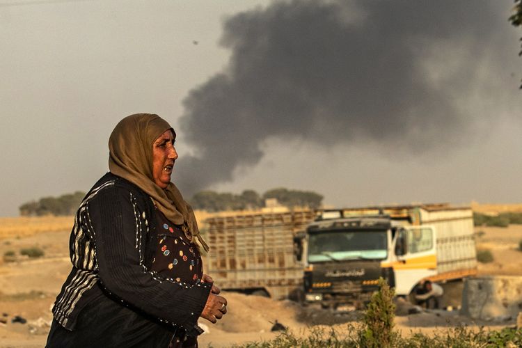 Seorang perempuan berjalan dengan di belakangnya kepulan asap hitam terlihat menyusul serangan yang dilakukan Turki terhadap Kurdi di Ras al-Ain di Provinsi Hasakeh, Suriah, yang berbatasan langsung dengan Turki pada 9 Oktober 2019.