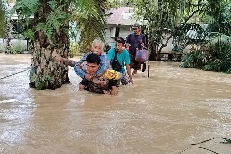 Petugas kepolisian saat mengevakuasi warga lansia dengan cara digendong menerobos arus banjir, di Kelurahan Kota Lama, Kecamatan Kunto Darussalam, Kabupaten Rokan Hulu, Riau, Minggu (28/1/2024).