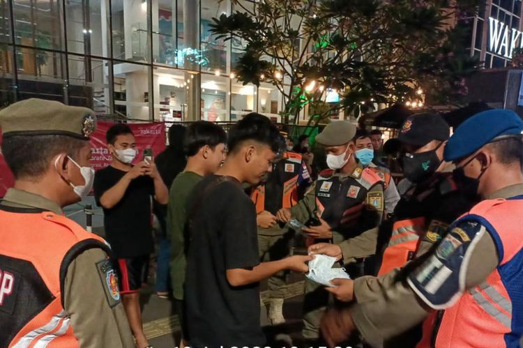 Satpol PP Jakarta Pusat membagikan masker ke remaja yang nongkrong di Dukuh Atas karena kerap melanggar protokol kesehatan, Senin (18/7/2022).