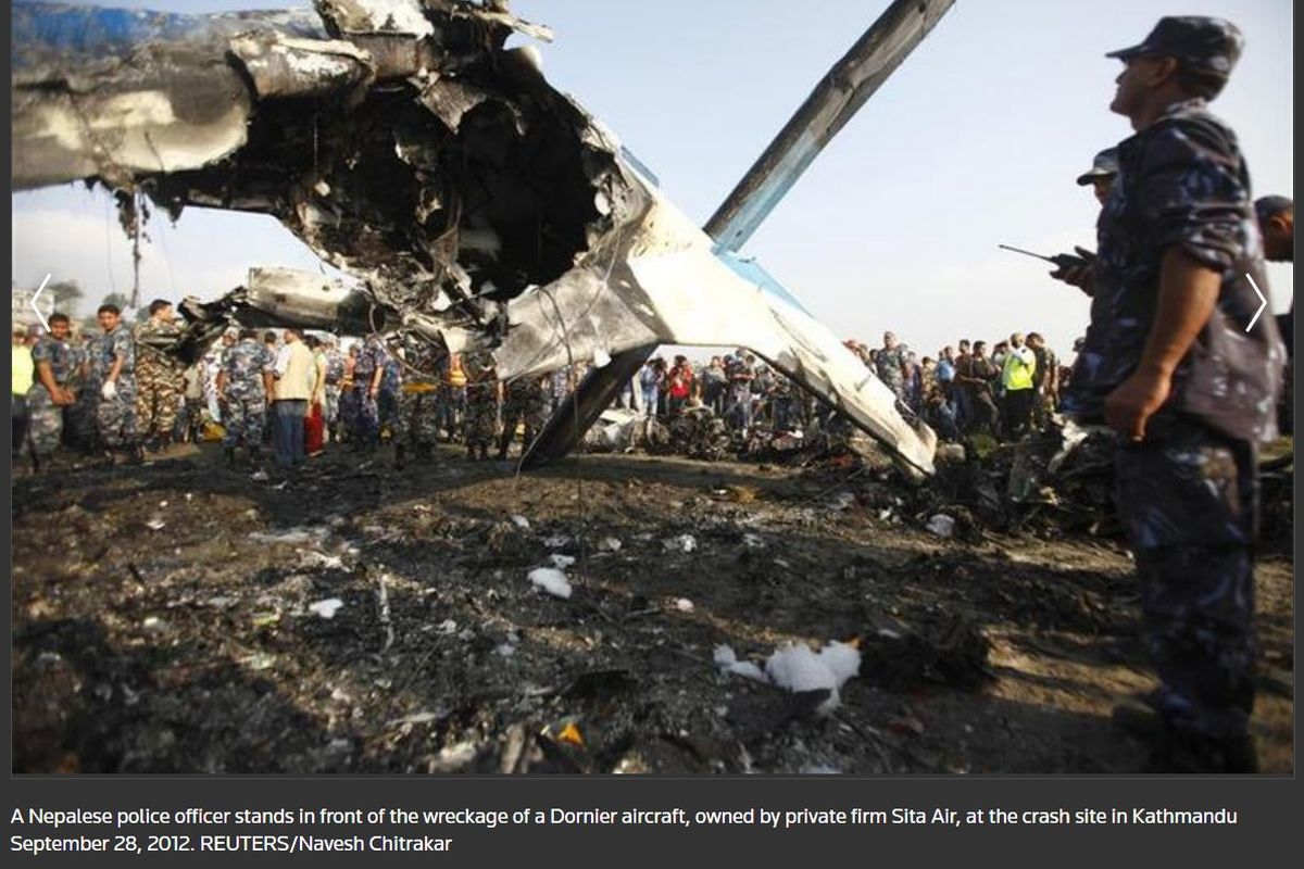 Foto dari Reuters memperlihatkan seorang polisi Nepal berdiri di depan reruntuhan pesawat Dornier, milik perusahaan swasta Sita Air, di lokasi kecelakaan di Kathmandu