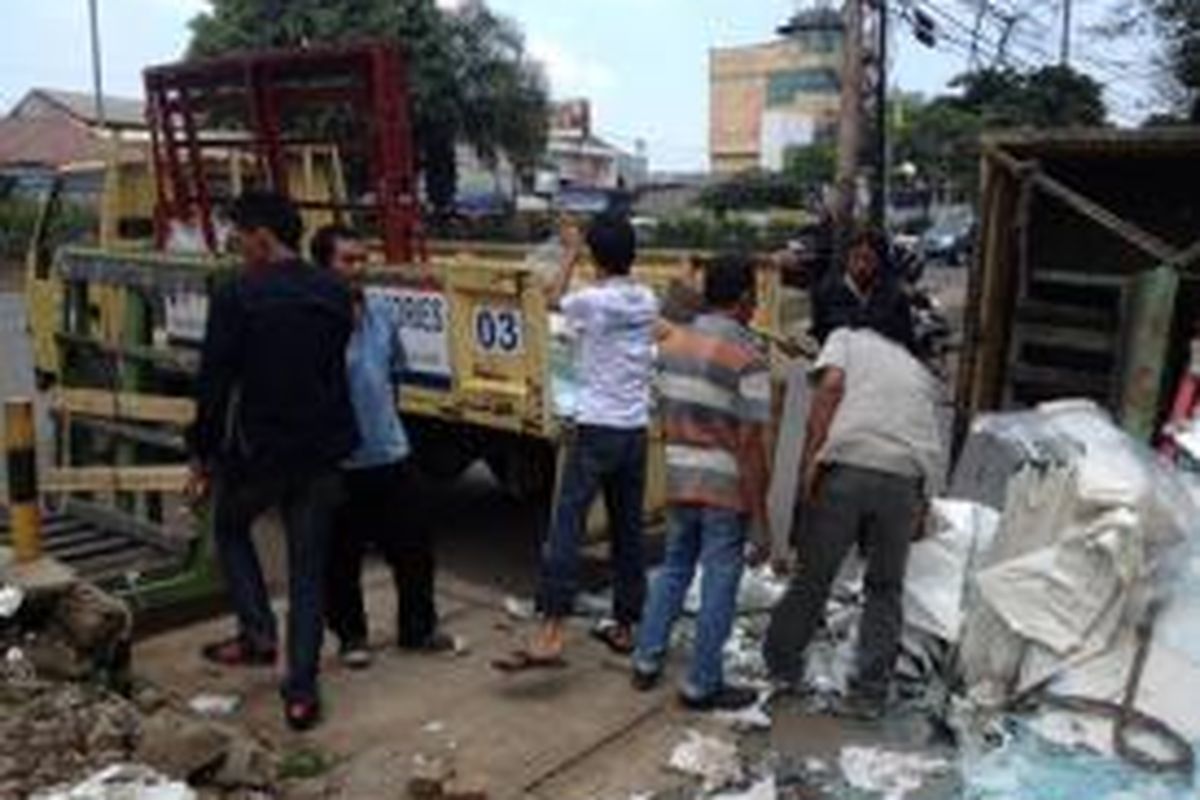 Pengemudi dan kenek dari truk kaca yang terguling memindahkan material-material kaca ke truk lainnya di Jalan Daan Mogot, Jakarta Barat, Senin (16/3/2015).
