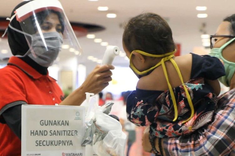 Seorang Petugas gerai pakaian di Mall Epicentrum Lombok, Selasa (19/5/2020) mengecek suhu tubuh balita yang dibawa ibunya belanja baju lebaran. Meskipun memakai masker anak anak rentan tertular covid19.