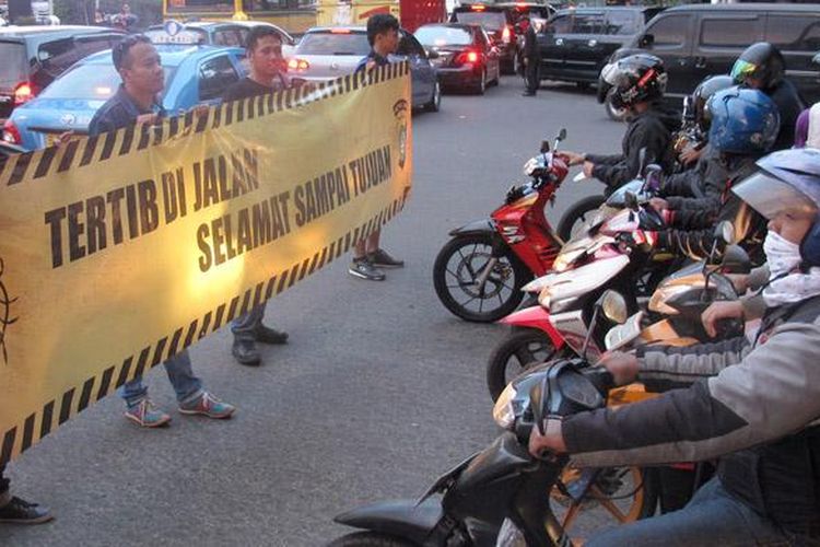 Para anggota komunitas membentangkan spandung imbauan pada pengendara sepeda motor.