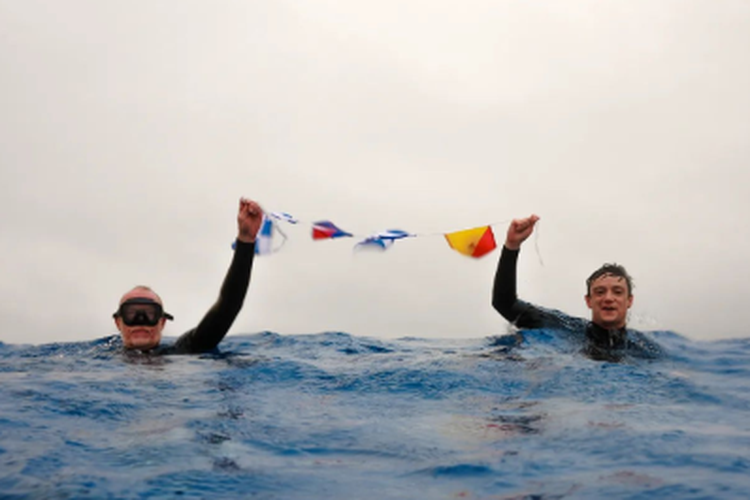 Chris Brown dan putranya, Mika, membentangkan bendera maritim bertuliskan NEMO saat berenang di Point Nemo, titik terpencil di Bumi
