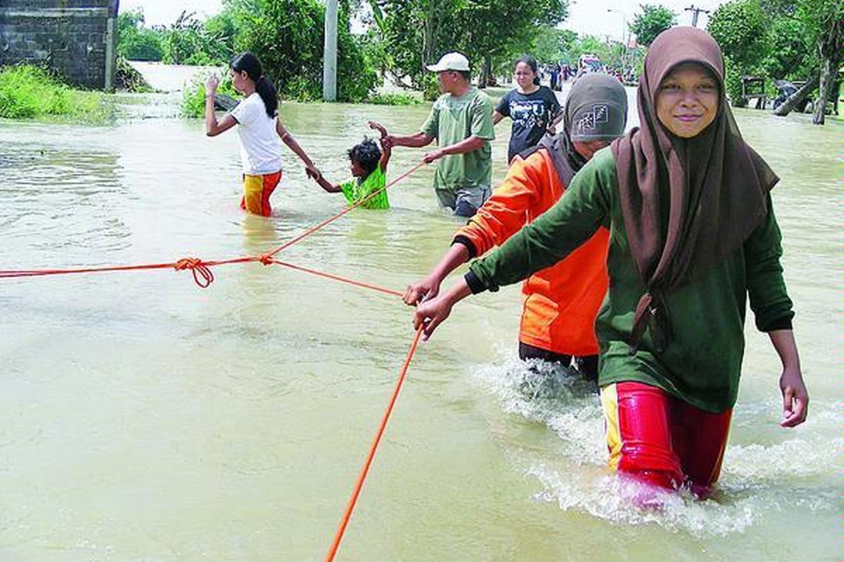 Warga berpegangan pada seutas tali saat berjalan melewati banjir luapan Kali Lamong di Desa Iker-iker Geger, Kecamatan Cerme, Kabupaten Gresik, Jawa Timur, Minggu (27/3).
