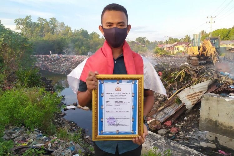 Amar Hawari (18) memperlihatkan piagam penghargaan sambil meletakkan bendera merah putih di pundaknya yang diselamatkan saat hanyut di parit pembuangan air di Jalan Rumbia Kota Selat Panjang, Kabupaten Kepulauan Meranti, Riau, Sabtu (15/8/2020).