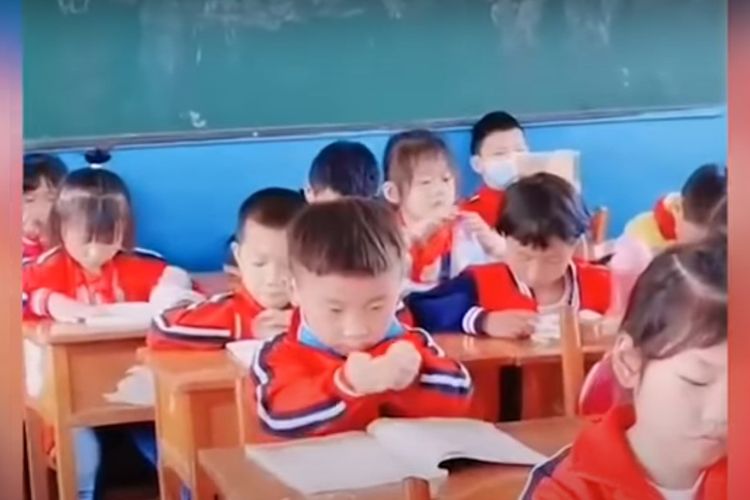 Tangkapan layar di video yang menunjukkan bocah SD di China membuat gerakan membasuh muka, untuk mengambil materi pelajaran di buku dan menuangkan ke kepalanya.