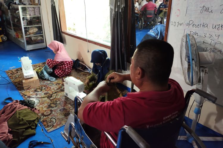 Pengguan kursi roda Daryono (55) tengah membantu proses belajar menjahit di Sanggar Kresna Patra yang didirikan Sri Setyaningsih (43) di rumahnya, Desa Klewor, Kecamatan Kemusu, Boyolali, Jumat (27/6/2025) pagi. Sanggar tersebut khusus memfasilitasi pelatihan busana, boga, dan pemasaran bagi para penyandang disabilitas dari berbagai daerah.