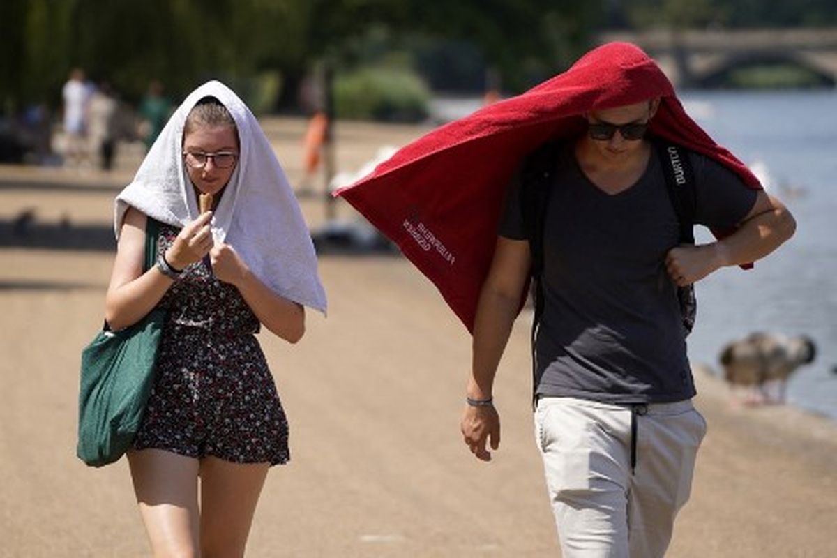 Orang-orang menutupi kepala mereka untuk berlindung dari matahari saat mereka berjalan melewati danau Serpentine di Hyde Park, London barat, pada 19 Juli 2022 saat negara itu mengalami gelombang panas yang ekstrem. 
