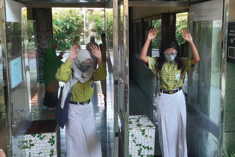 Para siswa kelas IX SMPN 4 Solo melewati bilik antiseptik yang terpasang di pintu masuk utama sekolah, Rabu (4/11/2020).